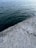 A concrete surface meets a body of water with gently rippling waves. The concrete is textured and weathered, showing signs of age and wear. The water is a deep blue-green color, suggesting depth and movement beneath the surface.