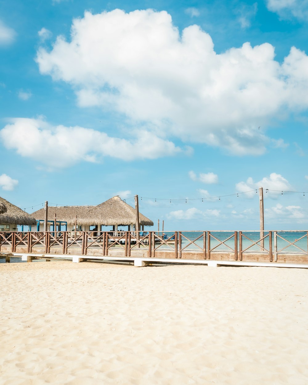 a sandy beach with a wooden fence and thatched umbrellas