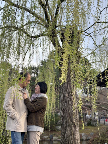 A quiet moment of siblings sharing a secret under a large oak tree.