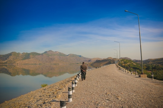 a man walking down a road next to a lake