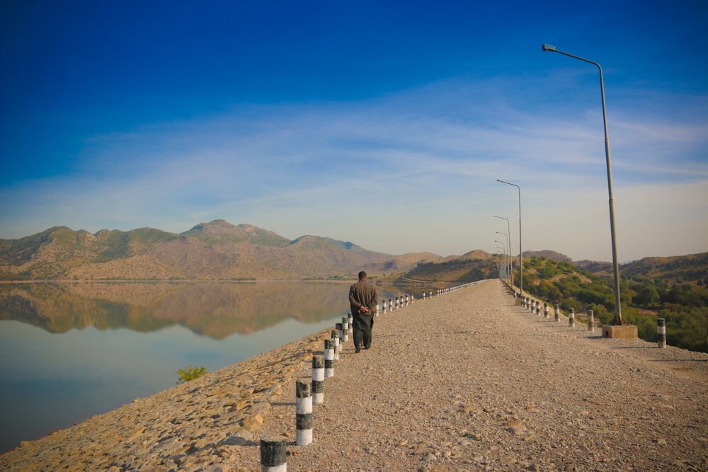 a man walking down a road next to a lake