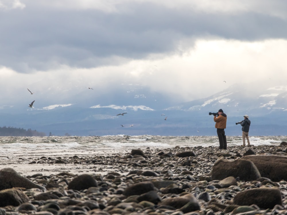 a couple of people standing on top of a rocky beach