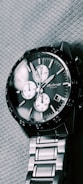 A silver chronograph wristwatch with a dark face and three subdials. It features a date window and has a metal link bracelet. The brand name on the face reads 'Octane Titan.' The watch is resting on a textured fabric surface.