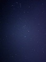 A dark, starry night sky with numerous small, twinkling stars scattered across the expanse. The image captures the vastness and mystery of the cosmos.