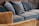 A collection of blue and brown sofas and cushions arranged in a cozy manner. The upholstery appears plush and soft, providing a comfortable seating area. The brown sofa outlines the foreground while the blue sofas and cushions dominate the background.