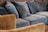 A collection of blue and brown sofas and cushions arranged in a cozy manner. The upholstery appears plush and soft, providing a comfortable seating area. The brown sofa outlines the foreground while the blue sofas and cushions dominate the background.