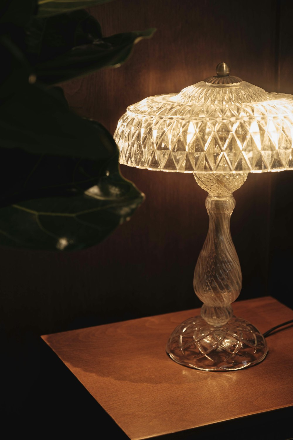 a glass table lamp sitting on top of a wooden table