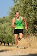 A dynamic shot of a man jogging outdoors wearing sporty clothes in green and blue tones.