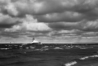 A detailed black and white photograph of a World War II battleship cutting through choppy seas under a cloudy sky.