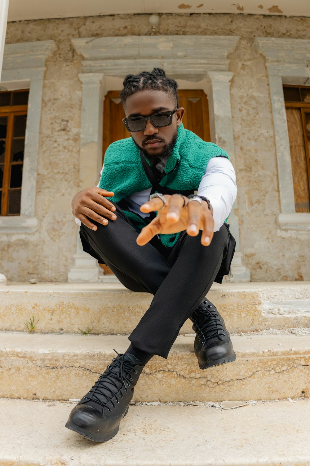 a man in a green vest and black pants sitting on steps