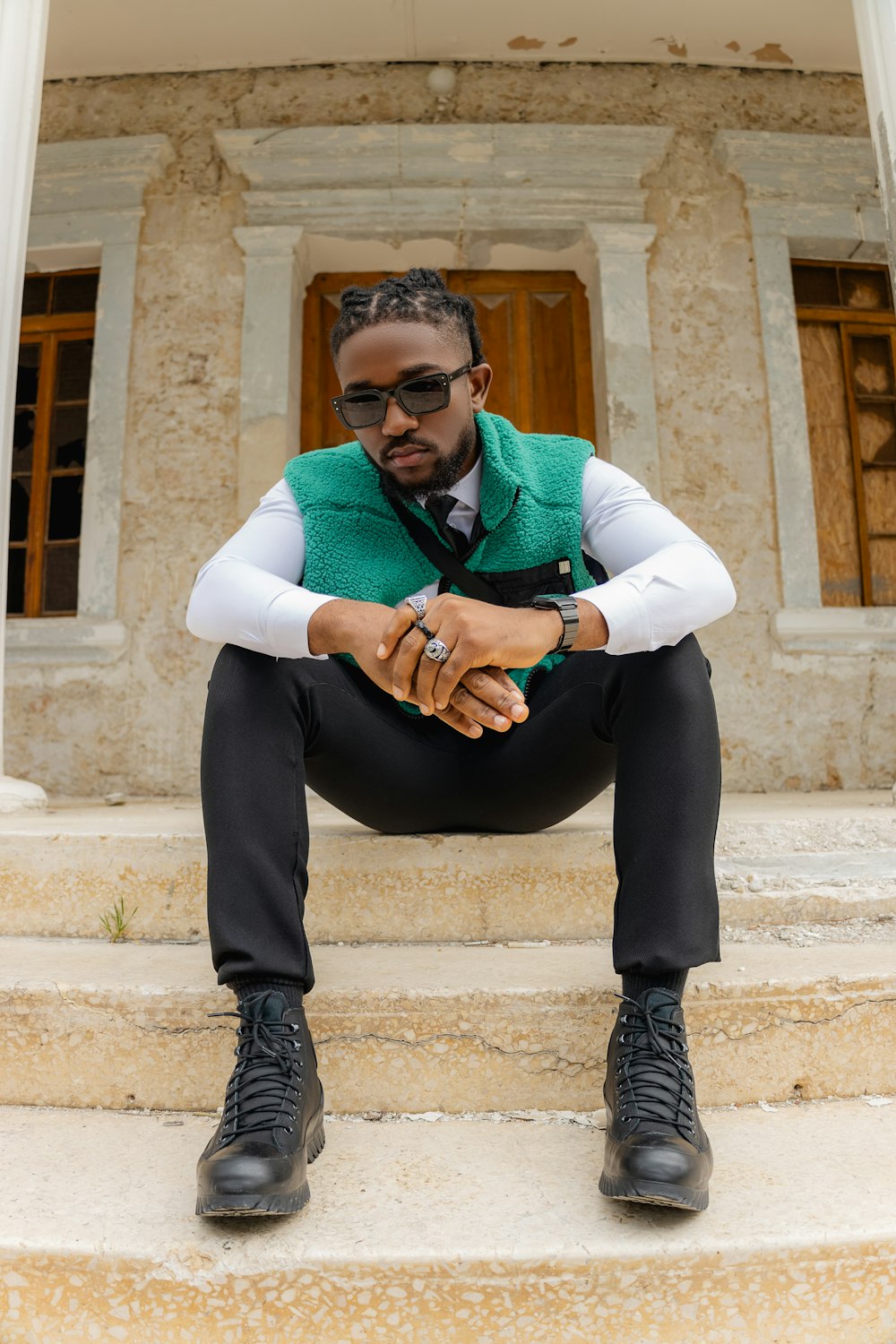 a man in a green vest and black pants sitting on steps