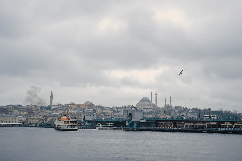 Boats docked on a lake with a mosque in the background, surrounded by clouds and