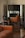A room with elegant vintage furniture, including a brown leather sofa and green upholstered chairs with wooden frames. The chairs are positioned in front of a large ornate mirror that reflects the room's interior.