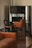 A room with elegant vintage furniture, including a brown leather sofa and green upholstered chairs with wooden frames. The chairs are positioned in front of a large ornate mirror that reflects the room's interior.