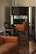 A room with elegant vintage furniture, including a brown leather sofa and green upholstered chairs with wooden frames. The chairs are positioned in front of a large ornate mirror that reflects the room's interior.
