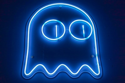 A blue neon sign resembling a ghost figure with two large circular eyes. The glow from the neon tubing creates a bright outline against a dark background.
