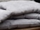 A stack of folded grey cushions placed on a wooden surface. The cushions have a textured fabric with visible seams and appear thick and comfortable.