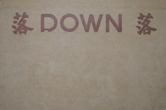 The image features the word 'DOWN' in bold, capitalized, red letters set against a textured, beige background. On either side of the word are red Chinese characters that add an additional element of cultural design.