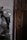 A power tool with a circular metallic blade is mounted on a wall inside a dimly lit workshop. The surroundings are rustic, showing a wooden door and several hanging objects. The surface of the wall is worn and uneven, contributing to the overall aged appearance of the setting.
