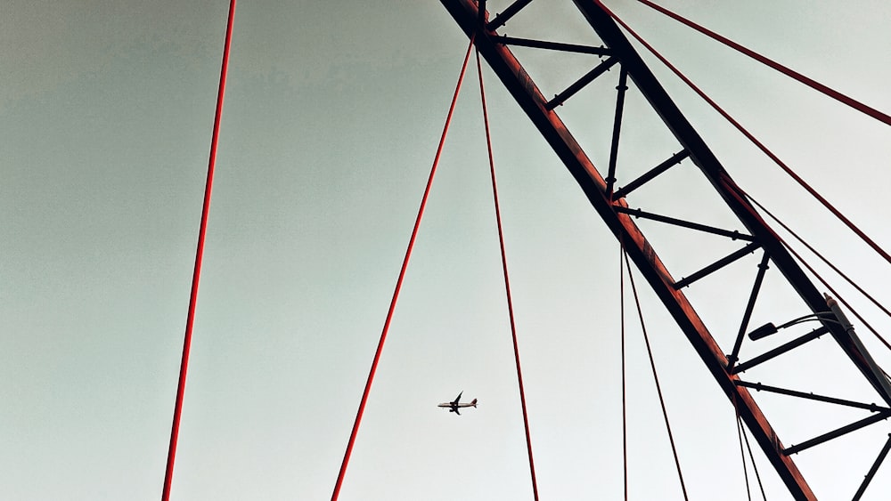 an airplane is flying over a bridge with red wires
