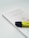 A book titled 'dê adeus ao excesso' by Fumio Sasaki lies on a light background. The book cover is minimalistic with soft colors, featuring a simple graphic. A yellow and black highlighter is placed on top of the book, positioned at an angle.