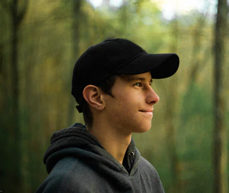 Side profile of a young person with a black Azor cap, city skyline blurred behind.