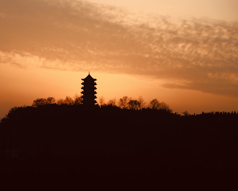 a silhouette of a pagoda on a hill at sunset