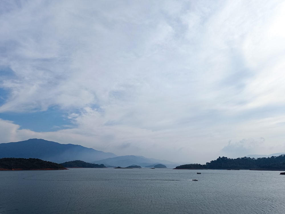 a body of water surrounded by mountains under a cloudy sky