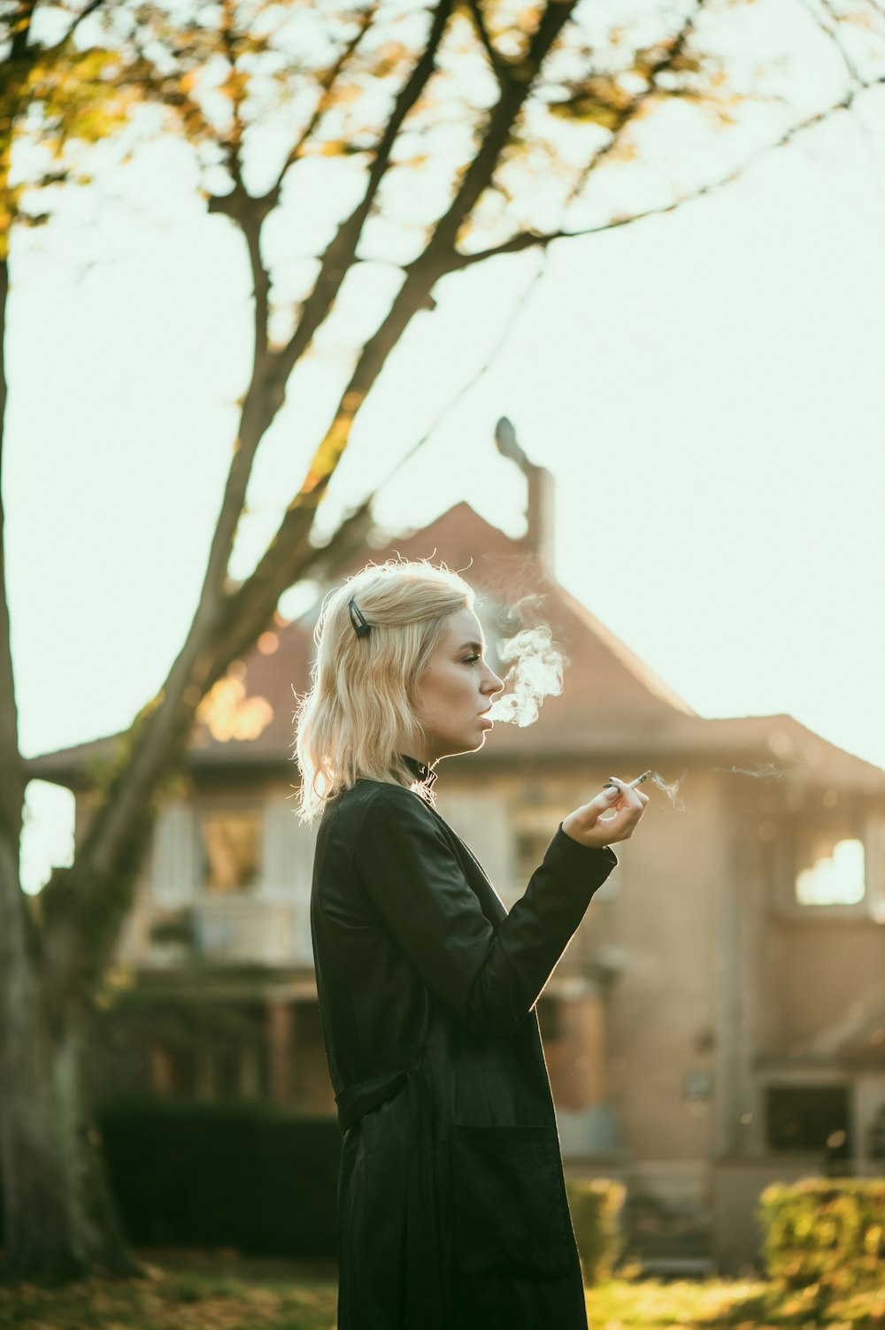 a woman standing in front of a tree smoking a cigarette