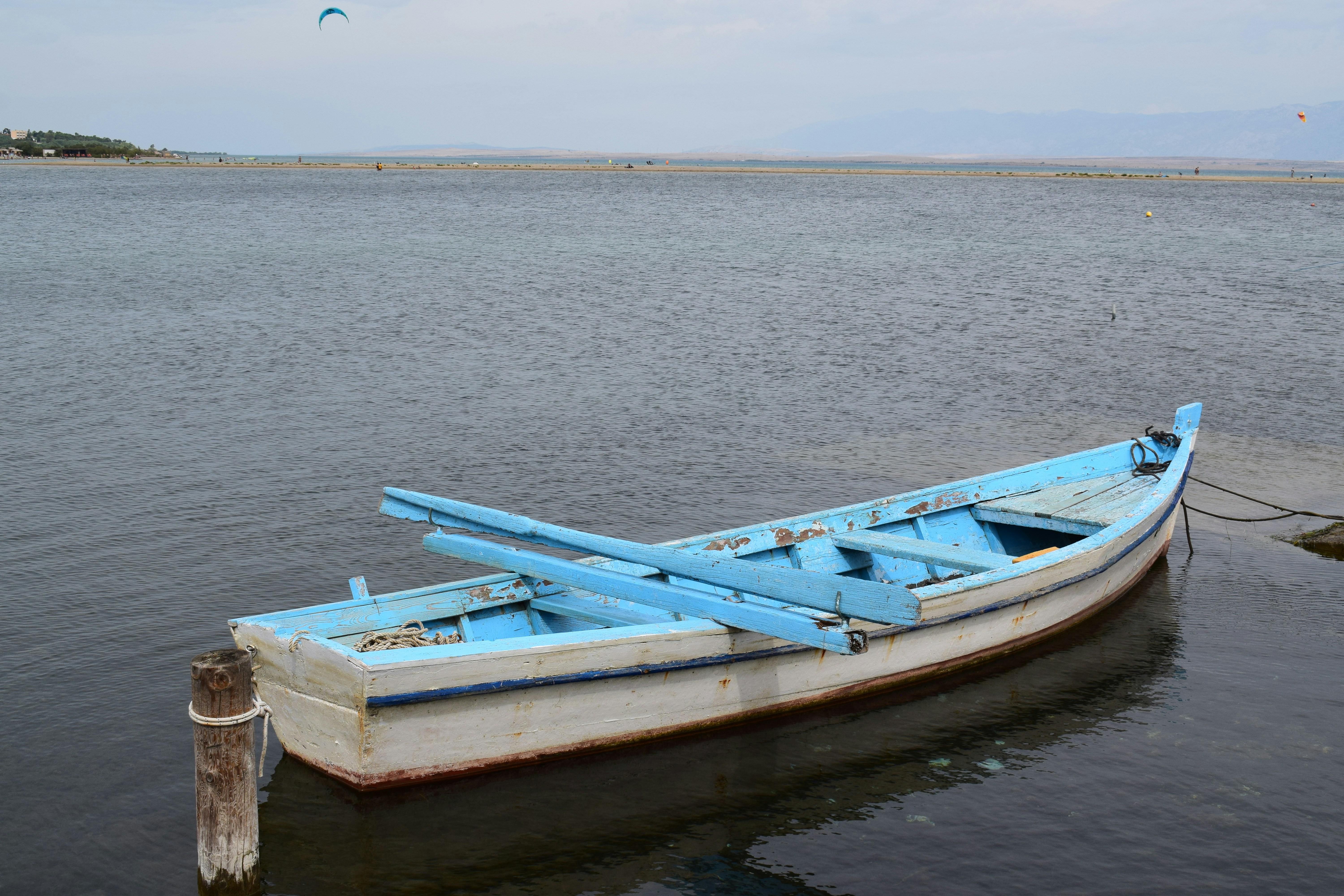 a blue and white boat sitting on top of a body of water, Old boat on shore.