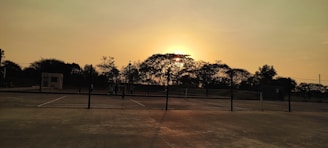 Wide view of a tennis court with players training at sunset.