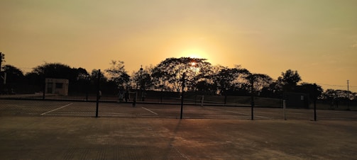 Wide view of a tennis court with players training at sunset.