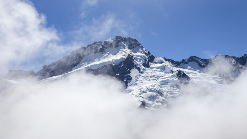 a mountain covered in snow and clouds under a blue sky