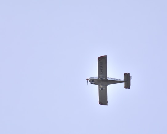 A small aircraft with visible registration markings flying against a clear blue sky.