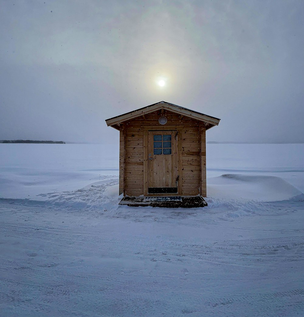 a small wooden shack sitting in the middle of a snow covered field