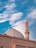 A mosque featuring a large domed roof and a single minaret with a crescent adornment. The building is set against a backdrop of vibrant blue skies with scattered white clouds.