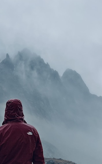 A hiker wearing a TrailDry jacket stands on a misty mountain ridge, raindrops visible on the fabric.
