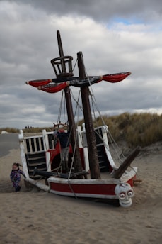 Children joyfully playing on a wooden pirate ship with sails and steering wheel inside a cozy play area.