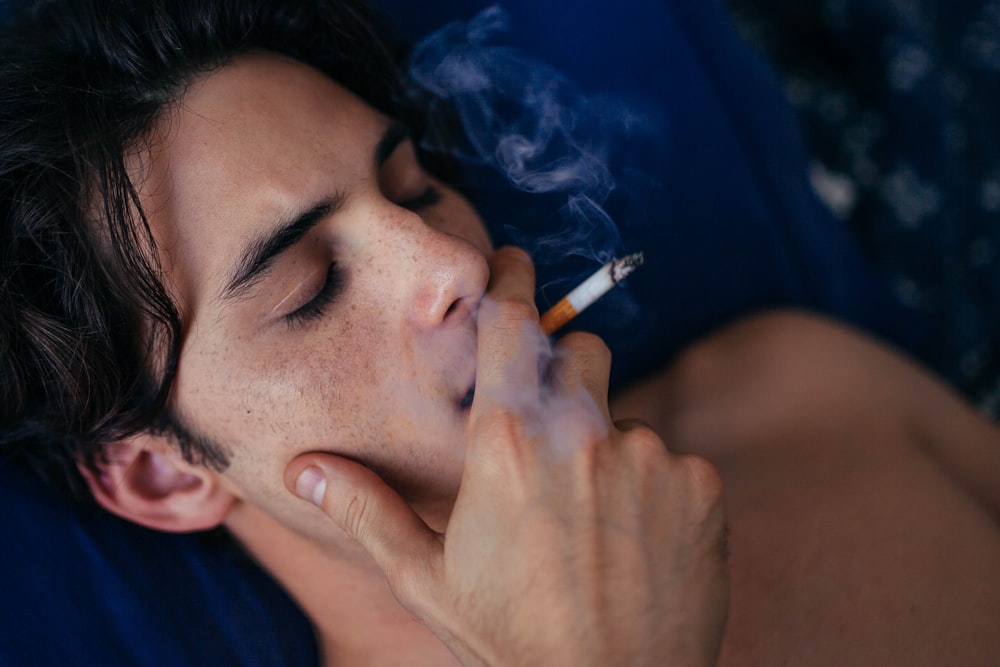a man laying on a bed smoking a cigarette