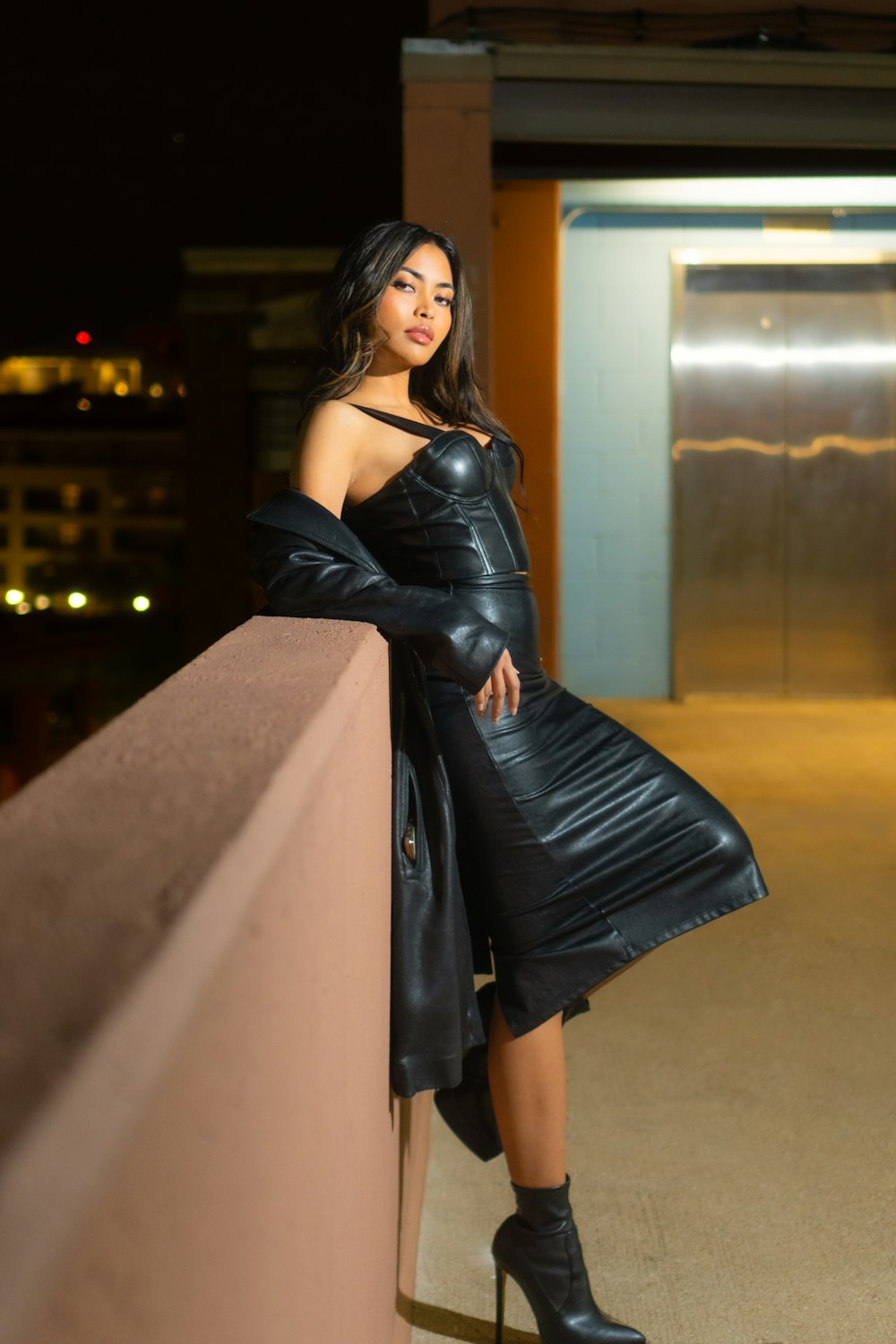 a woman in a black leather dress leaning on a wall