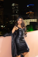 A stylish model wearing a sleek black Lumina Apparel dress in a softly lit urban setting.