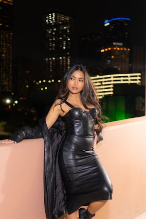 A stylish model wearing a sleek black Lumina Apparel dress in a softly lit urban setting.