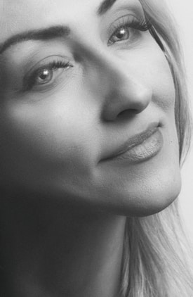 A close-up black and white portrait of a person with an expression that conveys calmness and introspection. The focus is on the eyes, which are looking upward, and the soft features of the face, with subtle details of the skin texture visible. Light plays gently across the image, enhancing the serene and thoughtful expression.