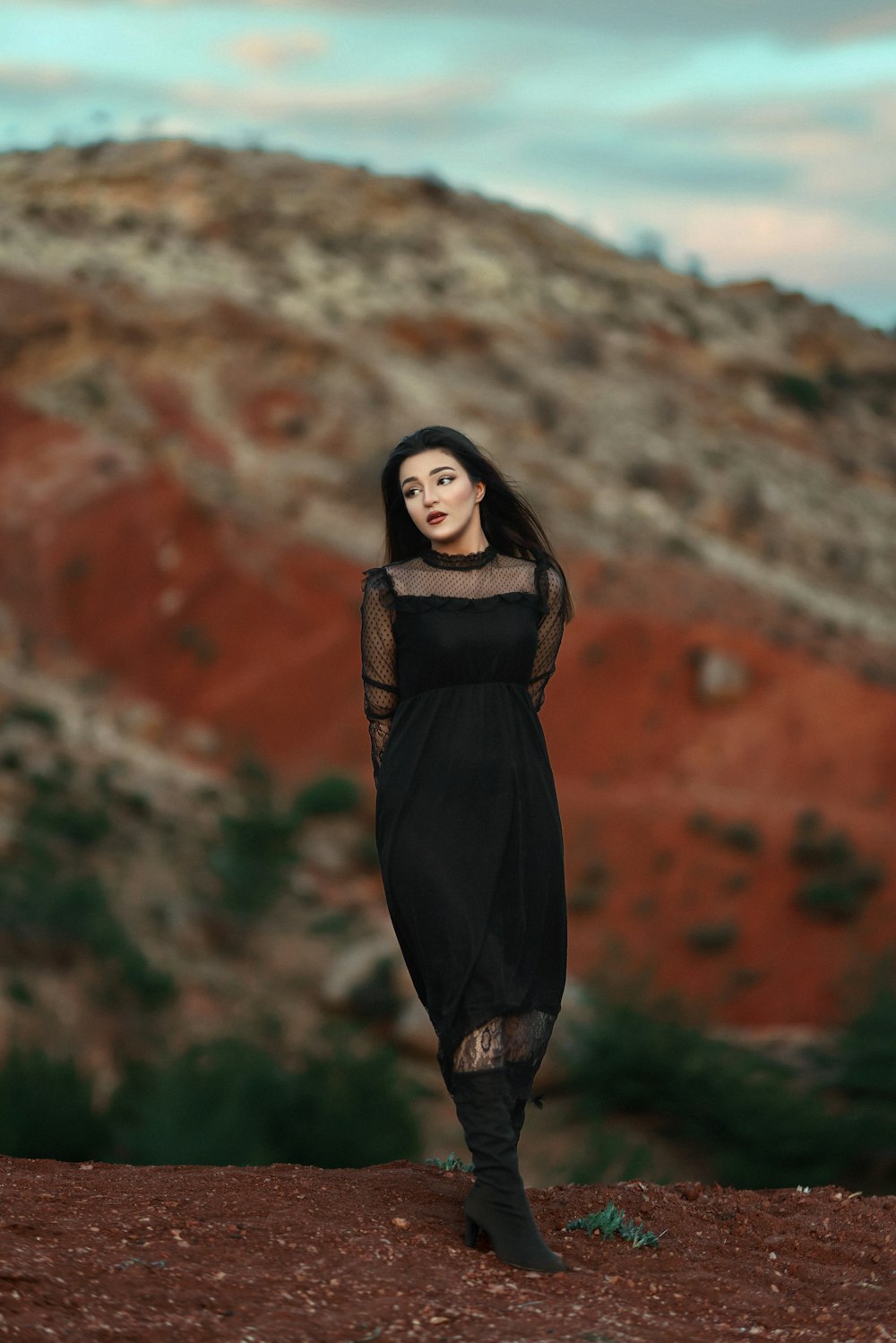 a woman in a black dress standing in front of a mountain