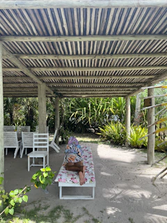 Softly lit photo of a flowing white pareô draped over a sun chair, with tropical greenery in the background.