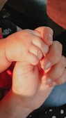 An adult hand gently holding a baby's hand, conveying a sense of care and protection. The nails are neatly manicured with a subtle glitter finish.