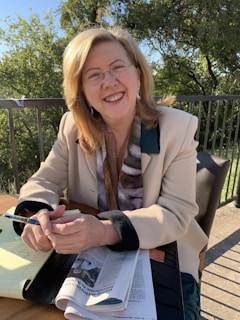 A confident woman standing in front of a modern office building, smiling and holding a notebook.