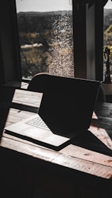 A sleek laptop resting on a raw wooden table inside a rustic cabin, sunlight filtering through.