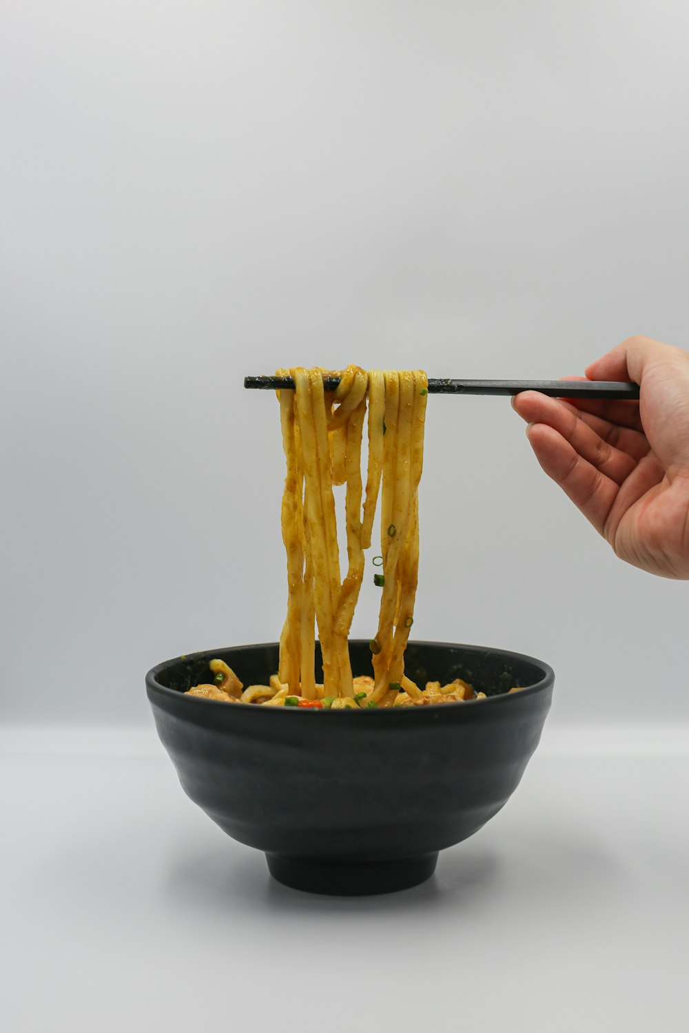 a person holding chopsticks over a bowl of noodles