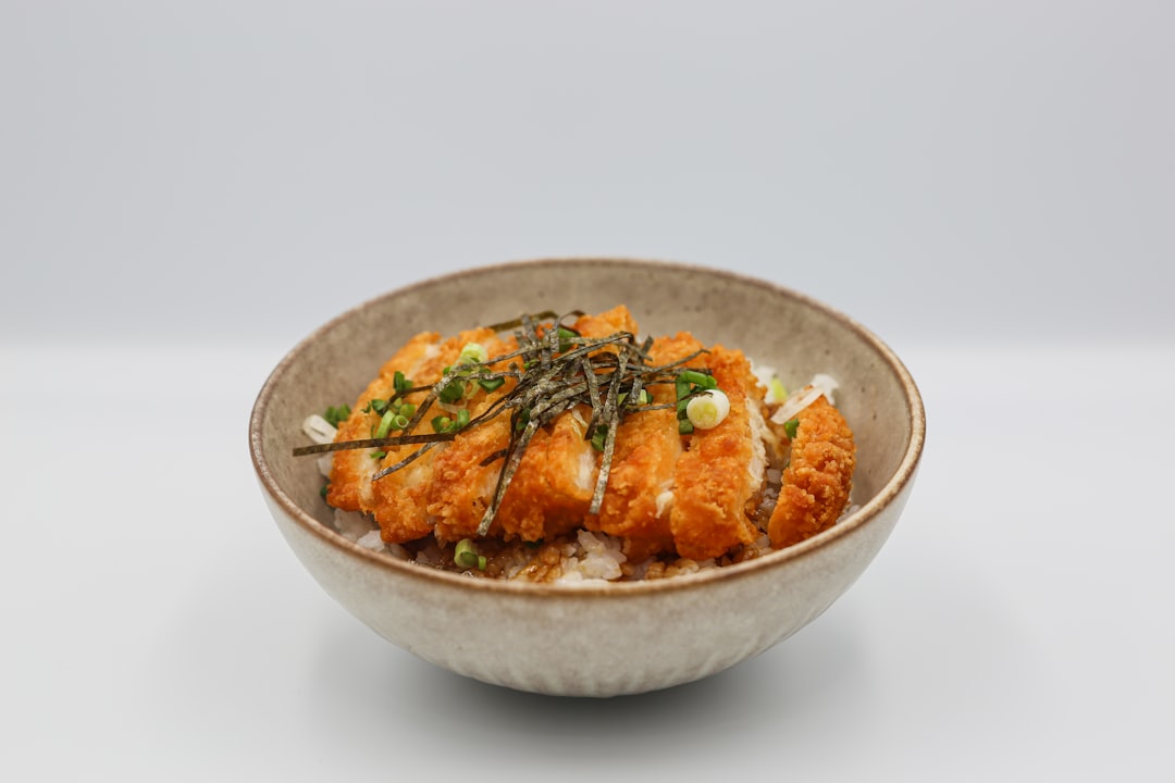 a bowl filled with rice and meat covered in sauce,